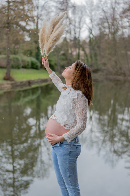 Rêveuse d'étincelles - Tatiana MAURINES - Photographe et rédactrice sur Écully, Lyon et la région Rhône-Alpes. Photographe de grossesse à Lyon, cette séance a été réalisée en extérieur près d'un étang. Une femme enceinte joue avec des graminés et le vent, une main posée sur son ventre.