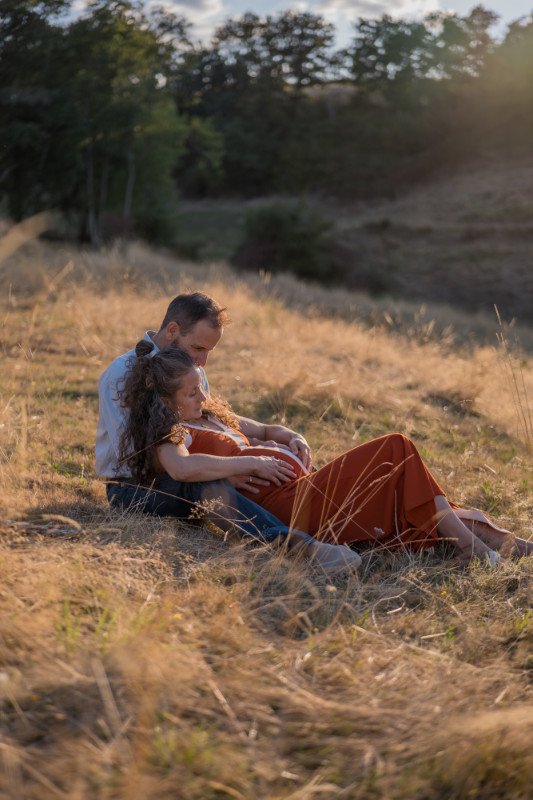 Rêveuse d'étincelles - Tatiana MAURINES - Photographe et rédactrice sur Écully, Lyon et la région Rhône-Alpes. Photographe de grossesse à Lyon, cette séance a été réalisée en extérieur, dans un champ. Un couple est assis dans un champ et caresse le ventre rebondit de la femme enceinte.