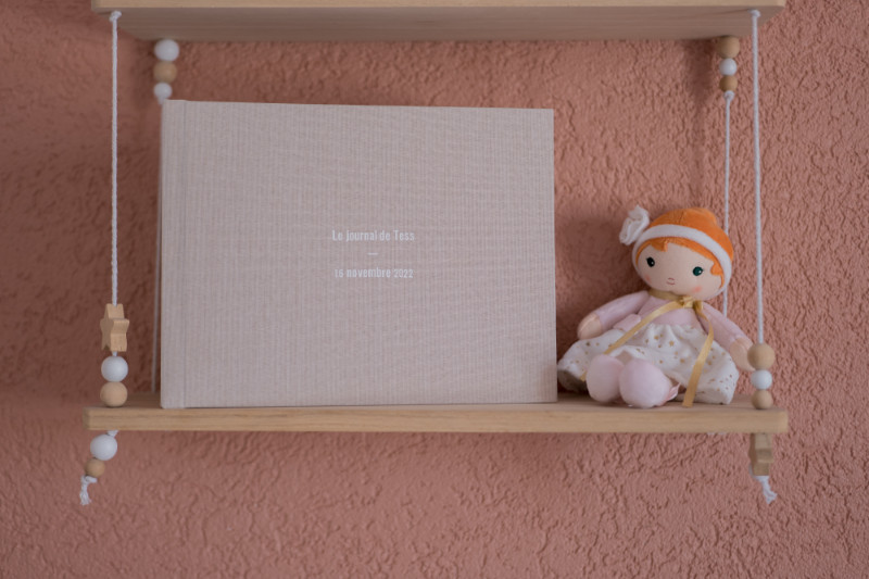 Rêveuse d'étincelles - Tatiana MAURINES - Photographe et conteuse sur Écully, Lyon et la région Rhône-Alpes. Photographe de grossesse à Lyon, je réalise aussi l'écriture du récit de naissance de votre enfant. Le journal d'un bébé est posé sur une étagère à côté d'une poupée.