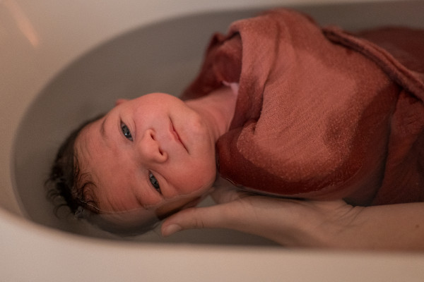 Rêveuse d'étincelles - Tatiana MAURINES - Photographe et biographe sur Écully, Lyon et la région Rhône-Alpes. Photographe à écully. Extrait d'une séance bain enveloppé. Un bébé baigne dans l'eau enroulé dans un lange.