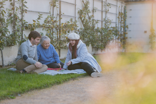 Rêveuse d'étincelles - Tatiana MAURINES - Photographe et rédactrice sur Écully, Lyon et la région Rhône-Alpes. Séance photo de famille à Lyon. Deux jeunes et leur grand-mère joue à un jeu de société assis dans l'herbe.